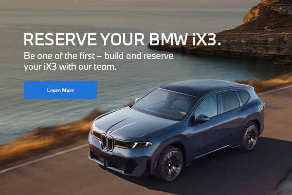 BMW iX3 vehicle driving on a road near mountains and water.
