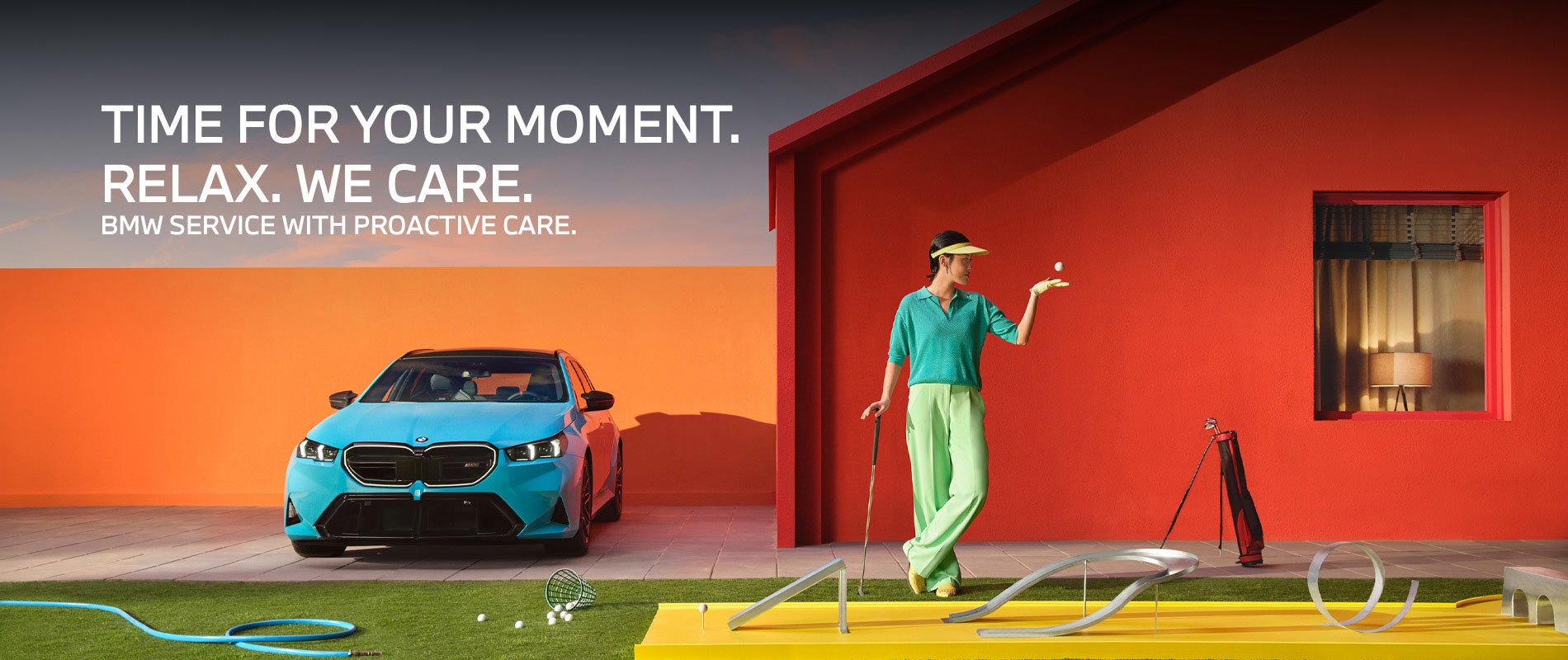 A BMW M5 Touring parked outside a home, with a person holding a golf club near a putting setup on the lawn.